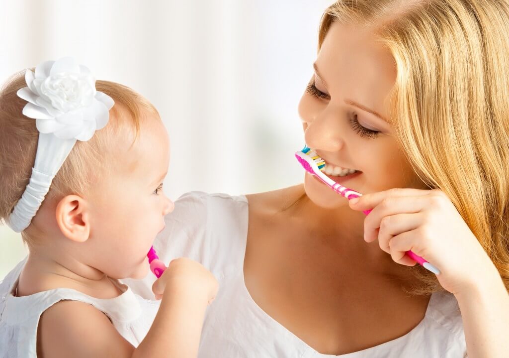 mama si fiica care se spala pe dinti cu periute de dinti roz si isi zambesc