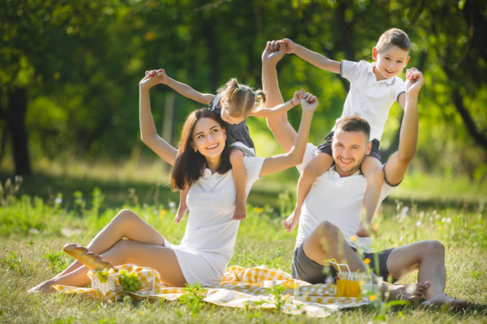 familie cu doi copii in parc la picnic pe paturica