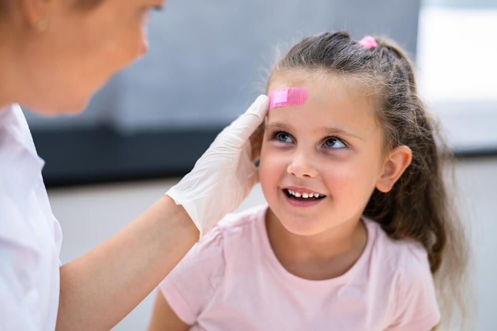 imagine copil cu plasture pe frunte pe care i-l pune o asistenta medicala