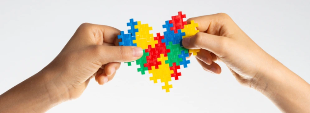 maini care tin un un puzzle colorat in forma de inima