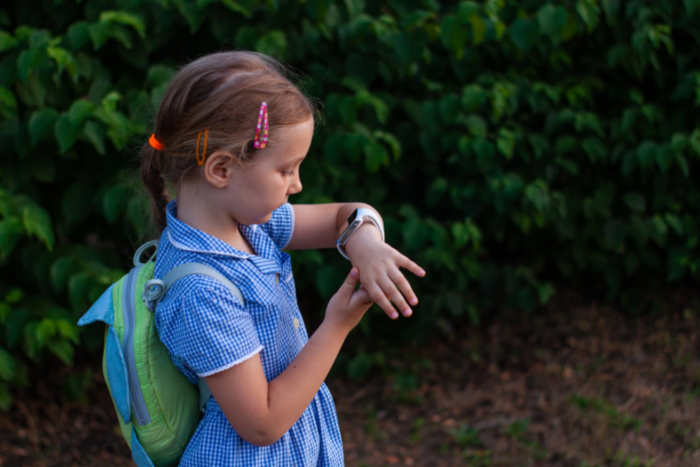 fetita care se duce la scoala cu ghiozdan in spate care se uita la ceasul de la mana care este un smartwatch empria pentru copii
