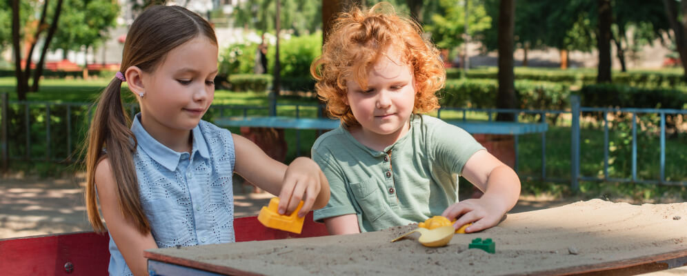 fetita si baietel care stau in parc si se joaca cu nisipul
