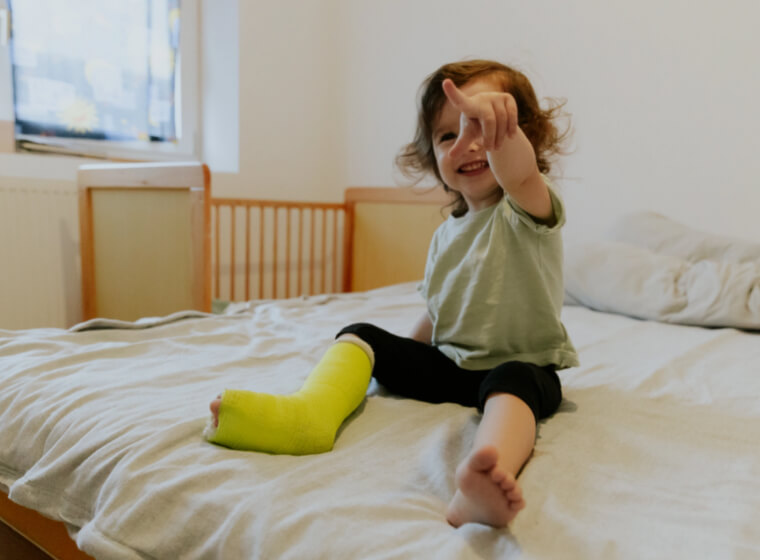 copil mic cu piciorul in ghips care sta in pat