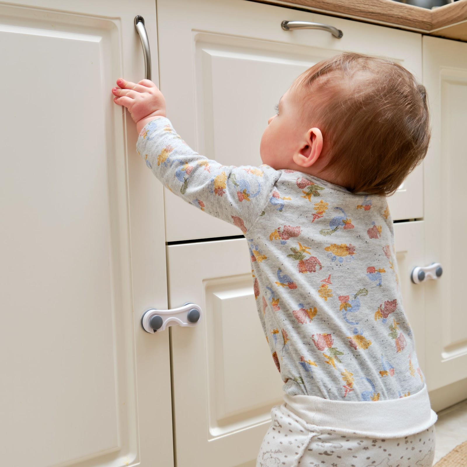 bebelus care incearca sa deschida usa unui dulap, blocata cu o siguranta pentru dulapuri