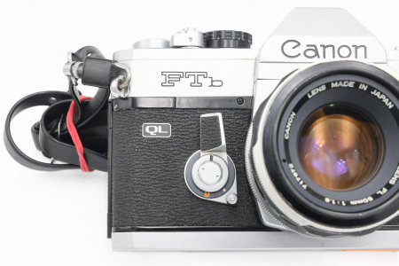 Kit aparat foto SLR pe film 35mm Canon FTb QL second hand în finisaj argintiu, cu obiectivul Canon Lens FL 50mm F1.8 montat și capacul frontal așezat alături pe fundal alb izolat. [2]