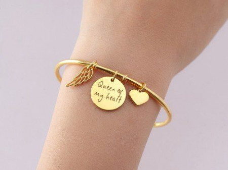 Brățări personalizate - O brățară aurie cu medalion gravat și charm-uri elegante, pe un fundal delicat.