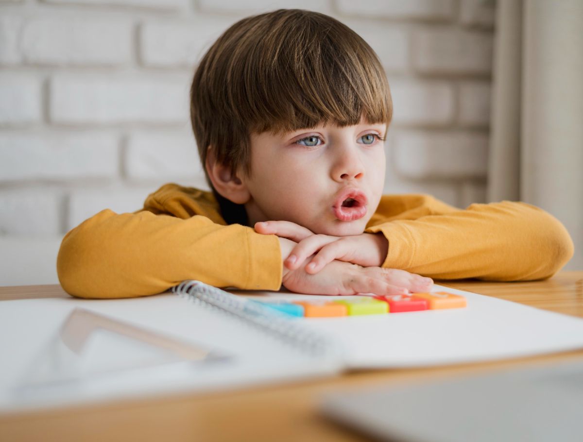 1. canabis in ADHD - baietel distras, caiet spirala, joc colorat, echer, hanorac galben-portocaliu, colt de laptop, fundal din caramizi albe