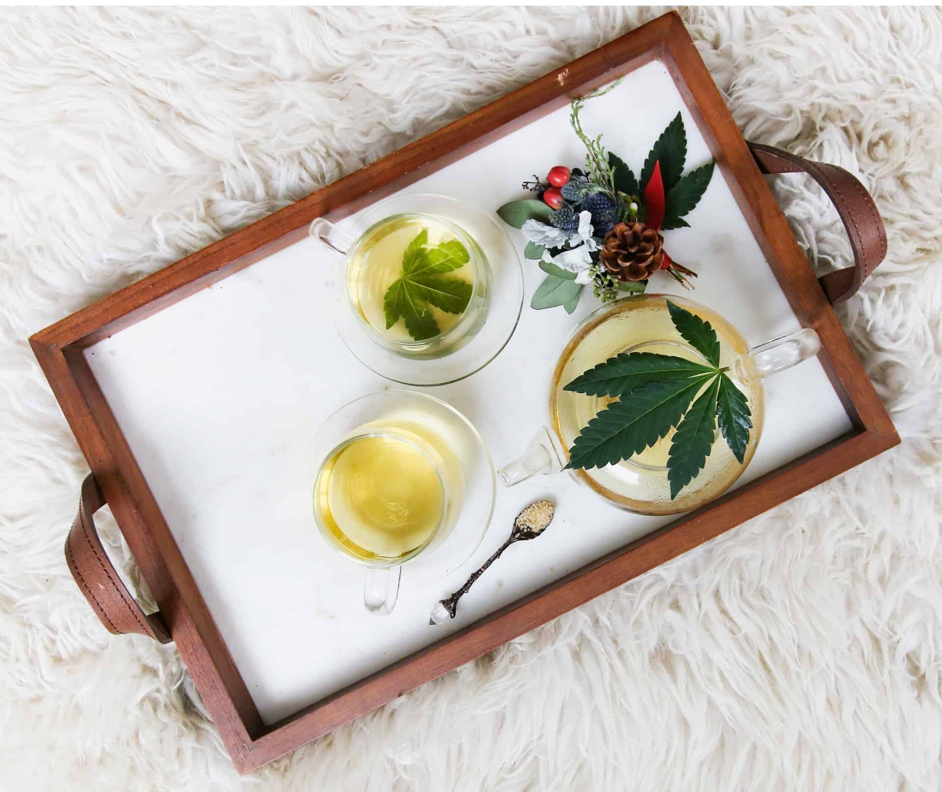4. Administrare ulei de canabis. tava cu cadru de lemn, cesti de ceai cu frunze in interior, lingurita, covor alb pufos
