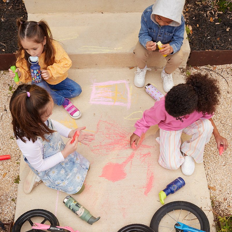 Patru copii desenând cu cretă pe asfalt, cu sticlele lor Kid Kanteen® alături