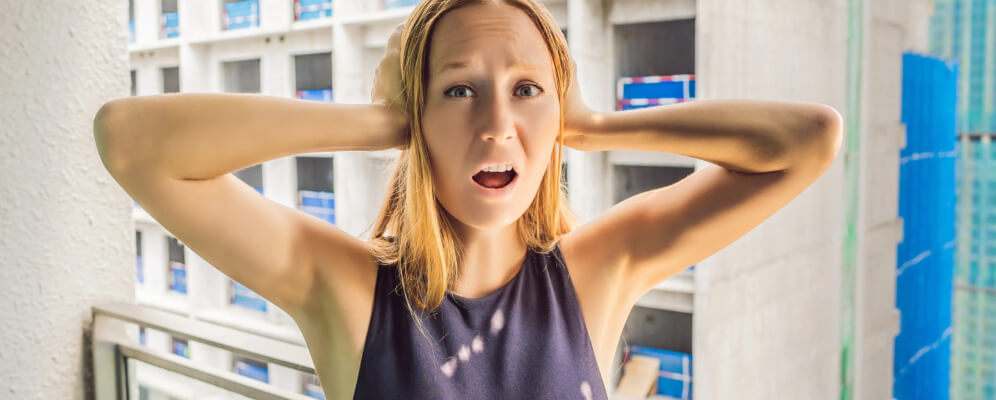 femeie pe balcon cu mainile la urechi ca sa nu mai auda zgomotul de afara