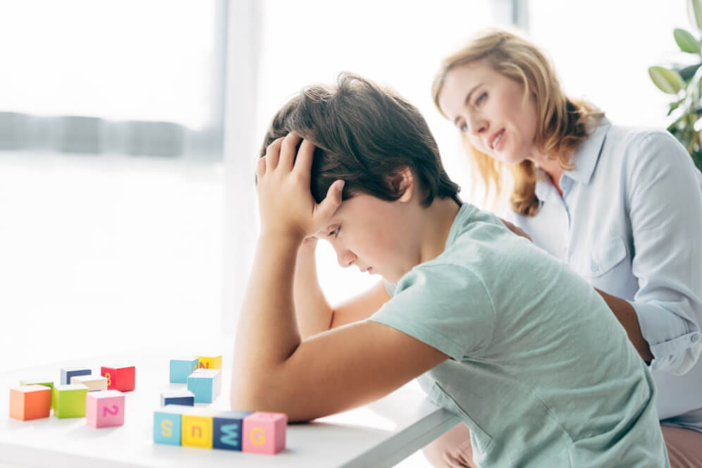 copil cu sindromul autism cu mainile la cap si cu tutorele in fundal 
