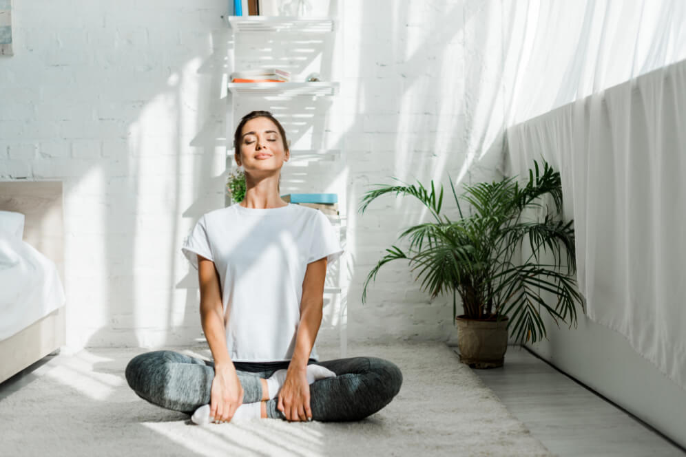 femeie fericita care sta in pozitie de lotus pe podea si mediteaza in liniste