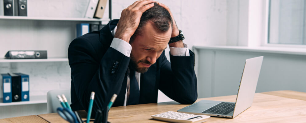 angajat la birou, stresat si obosit sta cu mainile in cap si se uita la laptop