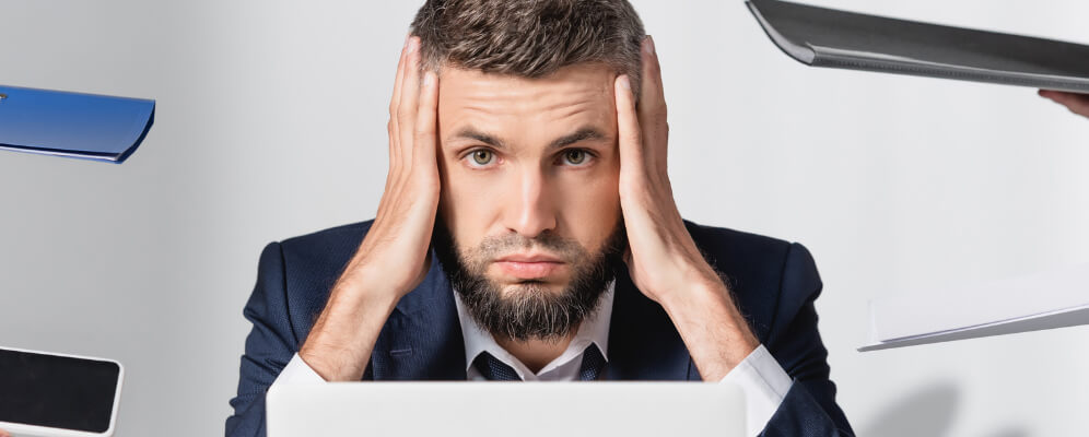 barbat in costum, la munca, cu multe sarcini de facut si cu mainile pe cap