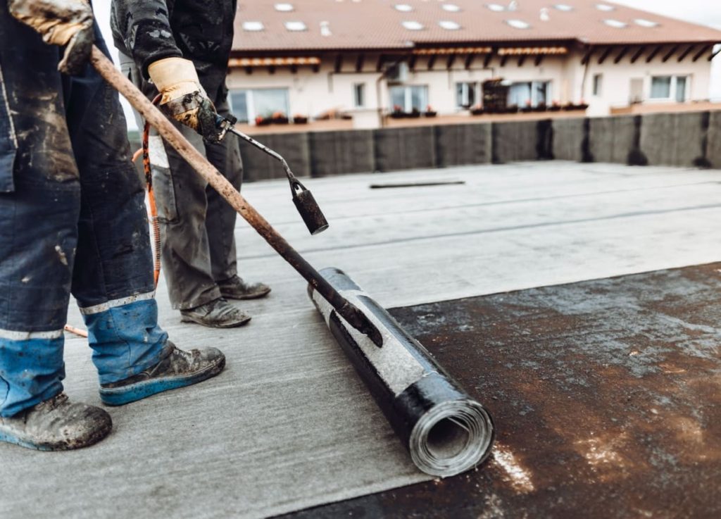 profesionisti care aplica membrana bituminoasa pentru a hidroizola un acoperis