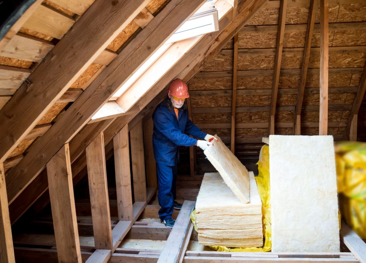 Un muncitor pune izolatie din vata de sticla in mansarda