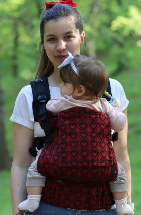 Marsupiu ergonomic Luna Una de culoare neagra, purtat de un părinte cu bebeluș. Design ajustabil, bretele moi și glugă pentru susținerea capului. [2]