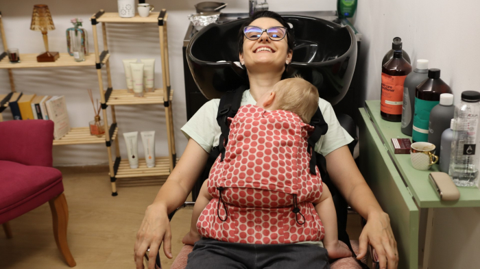 Marsupiu ergonomic Luna Una de culoare neagra, purtat de un părinte cu bebeluș. Design ajustabil, bretele moi și glugă pentru susținerea capului. [3]