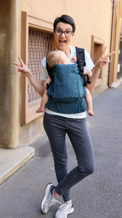 Marsupiu ergonomic Luna Una de culoare neagra, purtat de un părinte cu bebeluș. Design ajustabil, bretele moi și glugă pentru susținerea capului. [2]