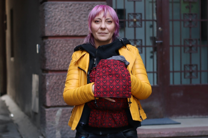 Marsupiu ergonomic Luna Una de culoare neagra, purtat de un părinte cu bebeluș. Design ajustabil, bretele moi și glugă pentru susținerea capului. [4]