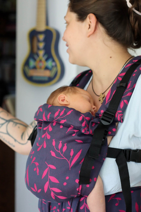 Marsupiu ergonomic Luna Una de culoare neagra, purtat de un părinte cu bebeluș. Design ajustabil, bretele moi și glugă pentru susținerea capului. [5]