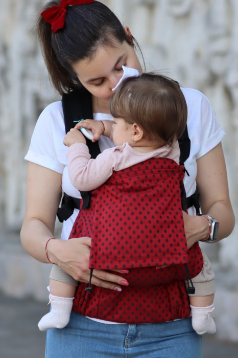Marsupiu ergonomic Luna Una de culoare neagra, purtat de un părinte cu bebeluș. Design ajustabil, bretele moi și glugă pentru susținerea capului. [2]