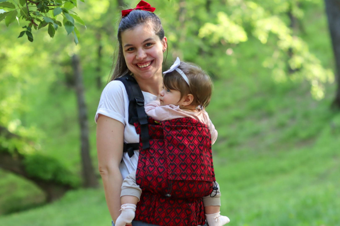 Marsupiu ergonomic Luna Una de culoare neagra, purtat de un părinte cu bebeluș. Design ajustabil, bretele moi și glugă pentru susținerea capului. [2]