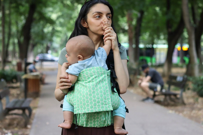 Marsupiu ergonomic Luna Una de culoare neagra, purtat de un părinte cu bebeluș. Design ajustabil, bretele moi și glugă pentru susținerea capului. [3]