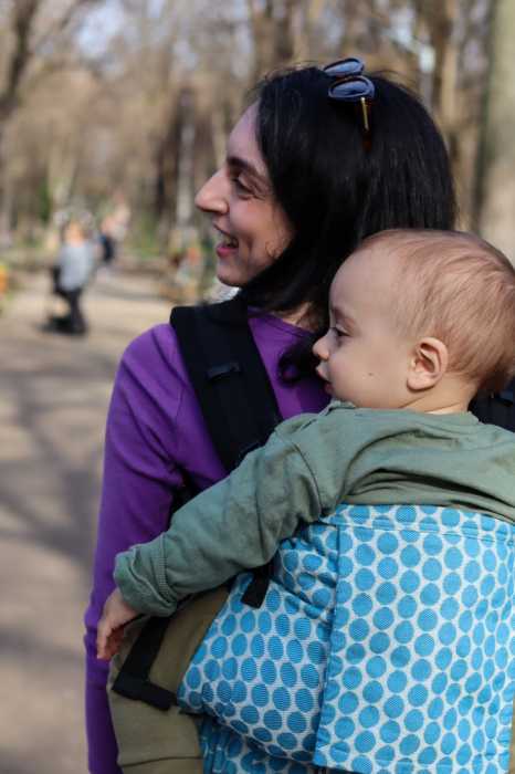 Marsupiu ergonomic Luna Una de culoare neagra, purtat de un părinte cu bebeluș. Design ajustabil, bretele moi și glugă pentru susținerea capului. [2]
