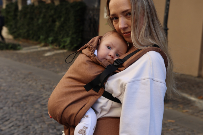 Marsupiu ergonomic Luna Una de culoare neagra, purtat de un părinte cu bebeluș. Design ajustabil, bretele moi și glugă pentru susținerea capului. [4]