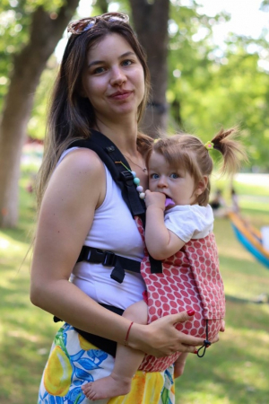 Babywearing - Marsupiu ergonomic Luna Una de culoare neagra, purtat de un părinte cu bebeluș. Design ajustabil, bretele moi și glugă pentru susținerea capului.