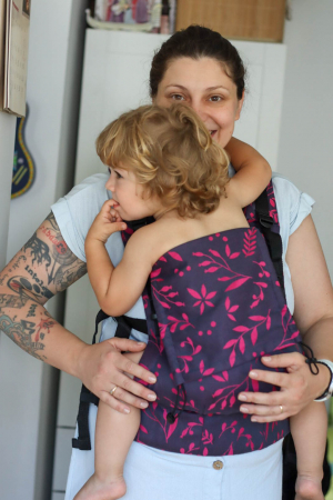 Marsupiu ergonomic Luna Una de culoare neagra, purtat de un părinte cu bebeluș. Design ajustabil, bretele moi și glugă pentru susținerea capului.