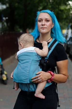 Luna UNA (0-36 Luni) - Marsupiu ergonomic Luna Una de culoare neagra, purtat de un părinte cu bebeluș. Design ajustabil, bretele moi și glugă pentru susținerea capului.