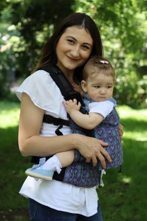 Luna UNA (0-36 Luni) - Marsupiu ergonomic Luna Una de culoare neagra, purtat de un părinte cu bebeluș. Design ajustabil, bretele moi și glugă pentru susținerea capului.