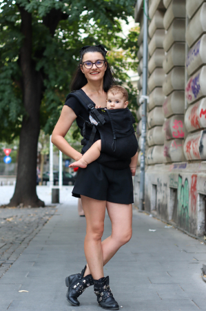 Marsupiu ergonomic Luna Una de culoare neagra, purtat de un părinte cu bebeluș. Design ajustabil, bretele moi și glugă pentru susținerea capului. [5]