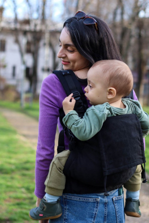 Marsupiu ergonomic Luna Una de culoare neagra, purtat de un părinte cu bebeluș. Design ajustabil, bretele moi și glugă pentru susținerea capului. [2]