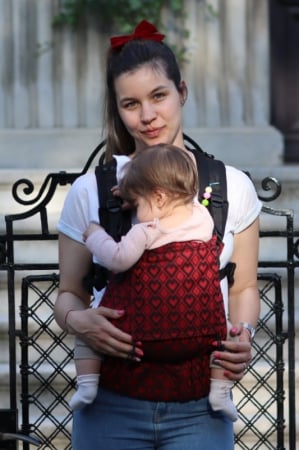 Luna UNA (0-36 Luni) - Marsupiu ergonomic Luna Una de culoare neagra, purtat de un părinte cu bebeluș. Design ajustabil, bretele moi și glugă pentru susținerea capului.