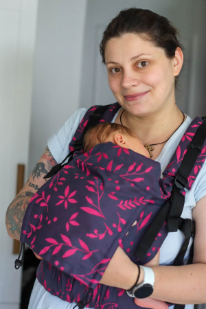 Marsupiu ergonomic Luna Una de culoare neagra, purtat de un părinte cu bebeluș. Design ajustabil, bretele moi și glugă pentru susținerea capului. [1]