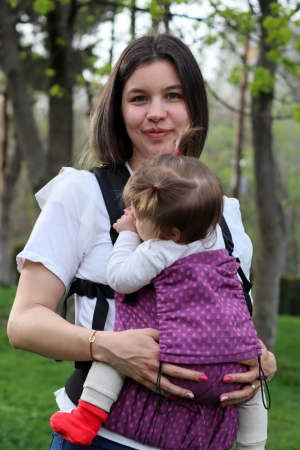 Babywearing - Marsupiu ergonomic Luna Una de culoare neagra, purtat de un părinte cu bebeluș. Design ajustabil, bretele moi și glugă pentru susținerea capului.