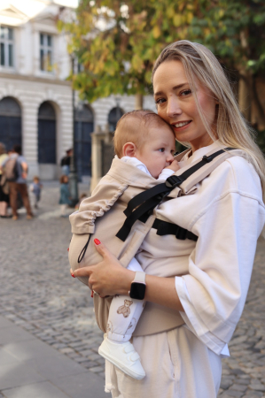 Marsupiu ergonomic Luna Una de culoare neagra, purtat de un părinte cu bebeluș. Design ajustabil, bretele moi și glugă pentru susținerea capului. [1]