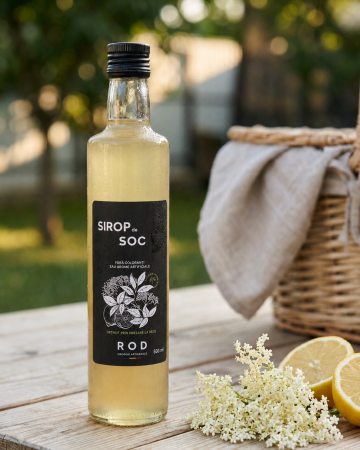 Sticla de Sirop de Soc ROD (500 ml) pe o masă de lemn, în lumina caldă de seară, lângă un zid cu trelaj.