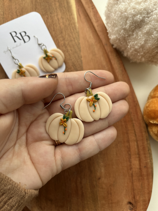 Cercei atârnați handmade cu dovlecei crem, fiecare decorat cu o floare delicată, din lut polimeric și tortițe din oțel chirurgical, inspirați de farmecul tomnatic. [1]