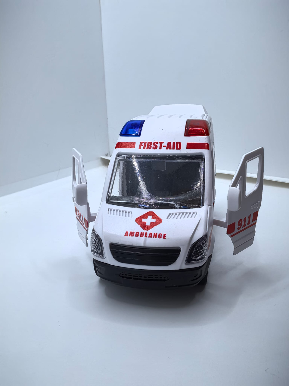 Mașinuță de jucărie ambulanță de culoare albă cu ușile din spate și portiera față deschise, inscripționată cu textul AMBULANCE URGENT. [3]
