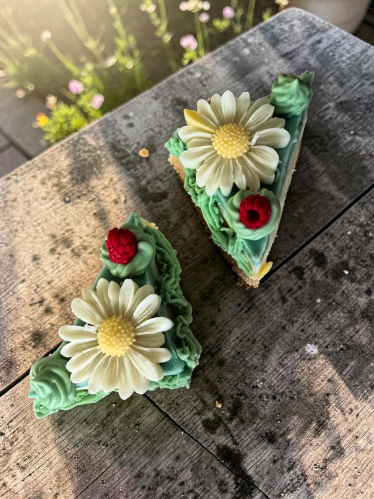 Lumânare artizanală din ceară de soia în formă de felie de tort, stratificată în galben, alb și turcoaz, decorată cu frișcă verde, o margaretă albă și o zmeură. [2]