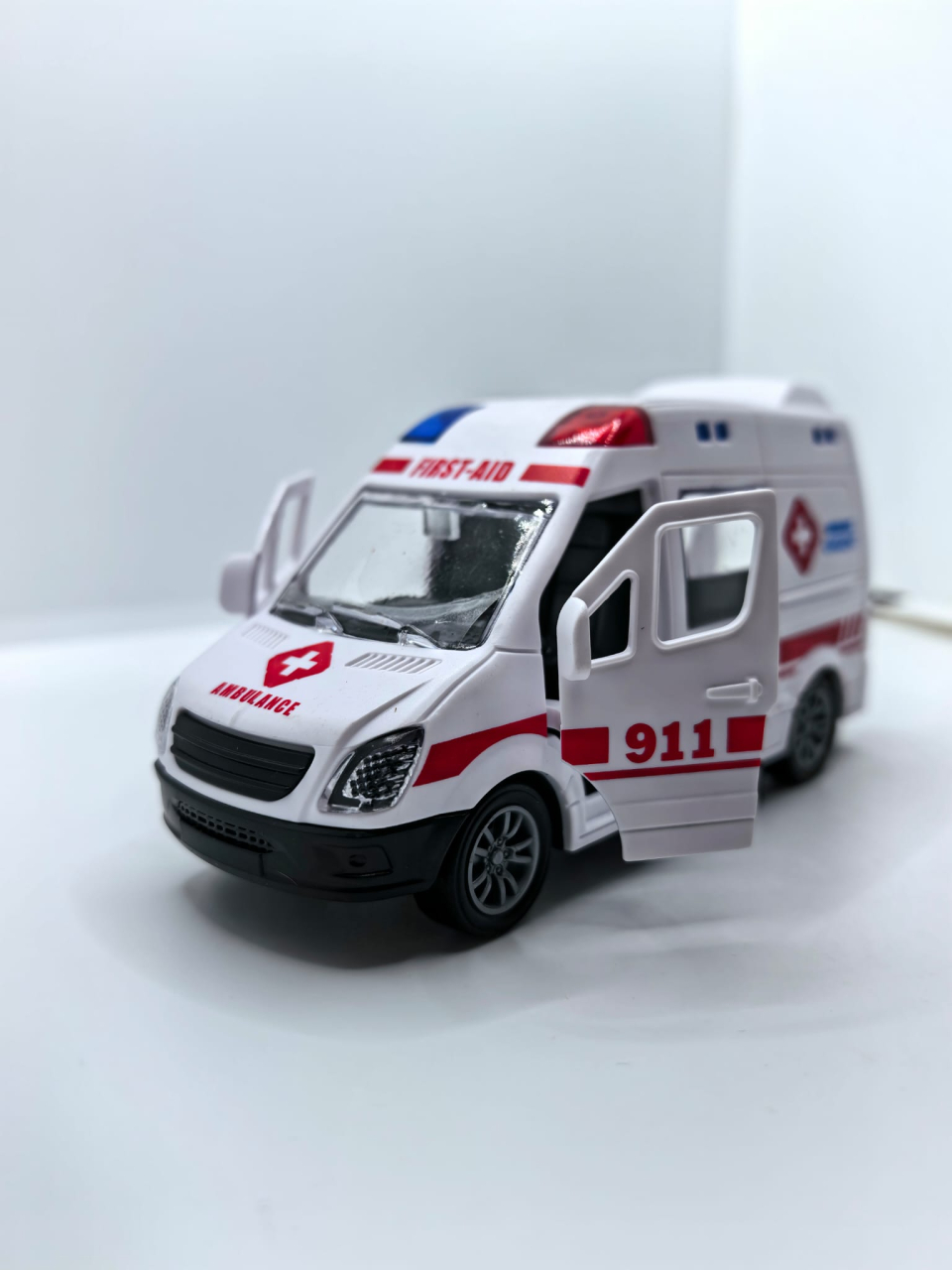 Mașinuță de jucărie ambulanță de culoare albă cu ușile din spate și portiera față deschise, inscripționată cu textul AMBULANCE URGENT. [2]