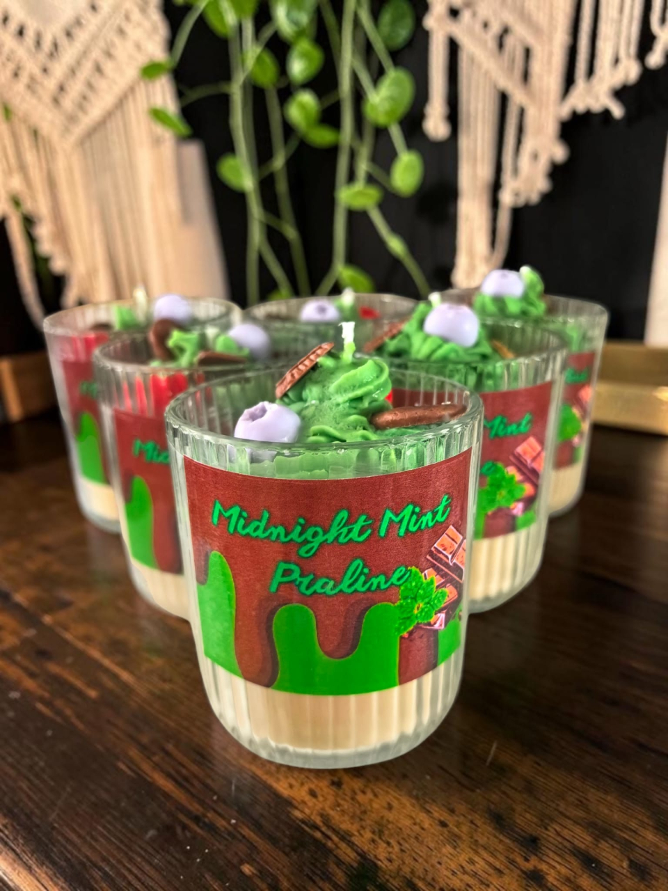 Grup de șase lumânări artizanale în pahare de sticlă striată, cu design de desert stratificat Midnight Mint Praline, având topping din ceară verde sub formă de frișcă și decorațiuni de fructe și ciocolată. [2]
