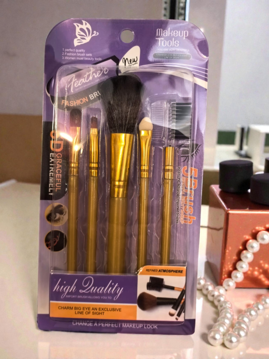 Set 5 pensule de machiaj negre cu ferule aurii, așezate ordonat pe un fundal neutru. [3]