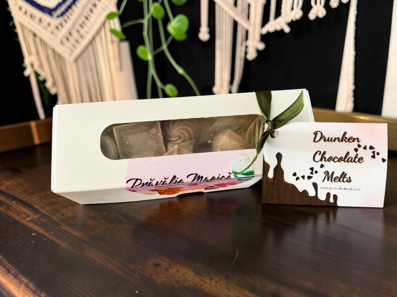 Cutie albă deschisă ce conține șase pastile de ceară parfumată (wax melts) din ceară de soia, cu design hiper-realist de praline de ciocolată în diferite forme geometrice. [3]