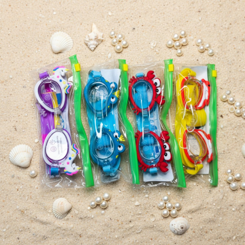 Ochelari de înot - Set de patru perechi de ochelari de înot pentru copii în huse cu fermoar, cu design de unicorn, crab și broscuță, așezați pe nisip decorat cu perle și scoici.