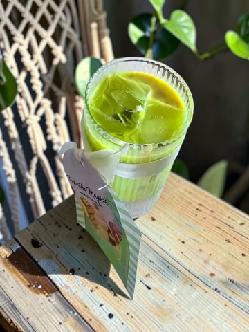 Delicii Parfumate: Lumânări Desert - Lumânare artizanală în pahar de sticlă texturată, cu ceară verde tip Matcha Latte și cuburi de gheață din ceară gel transparentă, decorată cu o etichetă Prăvălia Magică.